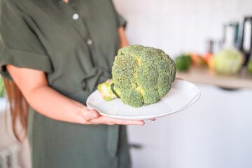 Close-up Fresh broccoli on a white plate in the hands of a woman in the kitchen. Dietetics, healthy...