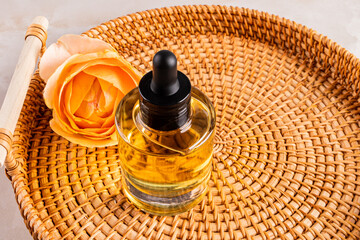 A natural cosmetic product, serum or oil in a glass bottle with a dropper stands on a wicker tray with a rose flower. A copy of the space. still life.