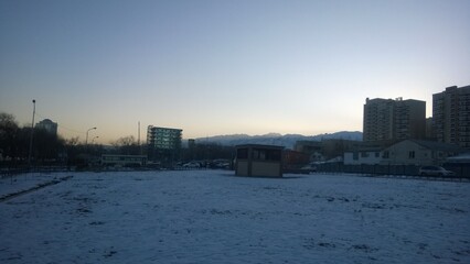 Snow-covered field and buildings under a cold, early morning sky.