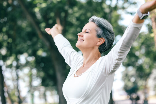 Joyful Mature Woman with Raised Arms and Closed Eyes Breathing Deeply in a Green Forest