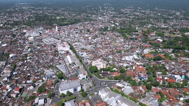 A cityscape of Salatiga with urban buildings in the foreground, framed by the majestic Mount Merbabu rising peacefully in the background under a clear sky.
