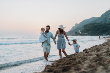 A family with two toddler children walking on beach on summer holiday at sunset.
