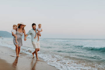 A family with two toddler children walking on beach on summer holiday at sunset.