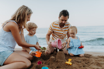 Two toddler children playing on sand beach with paretns during summer holiday.