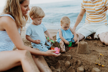Two toddler children playing on sand beach with paretns during summer holiday.