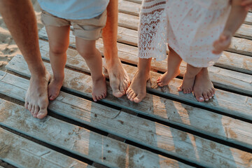 Legs and feet of family standing on beach on wooden walkway.