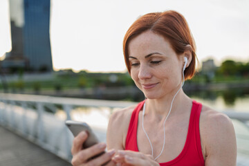 Runner playing music on a smartphone during her morning run across a city bridge.