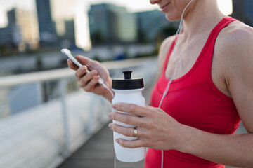 Runner checking her performance on a smartphone during her morning run across a city bridge.