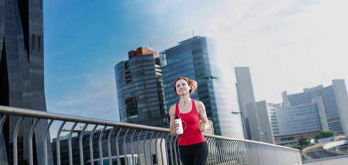 Woman resting after her morning workout, drinking water on a city bridge