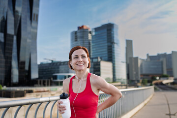 Woman resting after her morning workout, drinking water on a city bridge