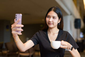 Young Asian woman sitting in coffee shop wearing black dress using phone