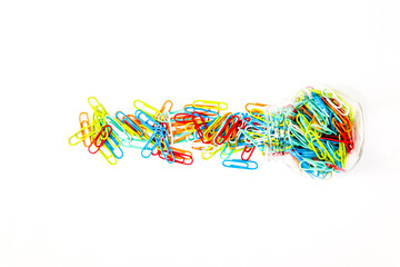 Colorful paper clips scattered from a glass jar on a clean white surface, creating a vibrant and...