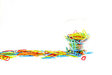 A vibrant collection of colorful paper clips spilled around a container on white background