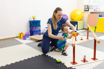 Young cute child practices standing and balancing using handrails with assistance from physical...