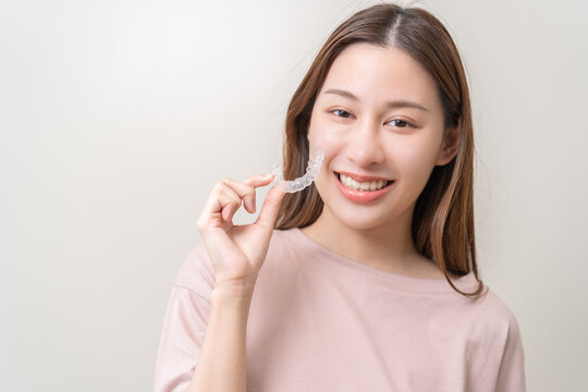 Dental invisible braces, beautiful smiling asian young woman holding invisalign braces, wearing orthodontic silicone trainer, white smile using invisible whitening tray. Stomatology, dental healthcare