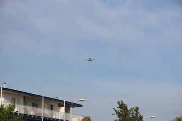 Avión despegando cerca de una zona de playa, con palmeras, farolas y casas costeras al fondo. La...