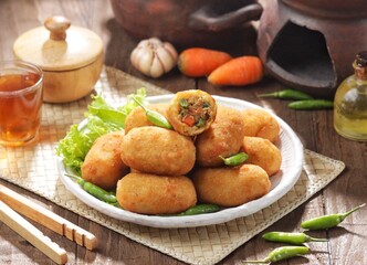 Kroket kentang. Croquettes are lumps of finely mashed potatoes filled with seasoned minced meat and mixed with vegetables such as carrots or green beans. The croquettes are coated with beaten egg and 