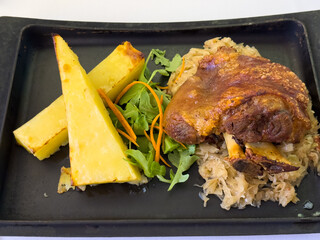 Roast pork knuckle with crispy skin, sauerkraut and gratin potatoes served on black tray....