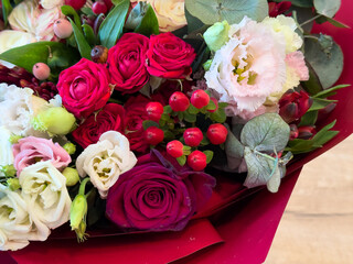 Closeup of colorful bouquet with roses, lisianthus, berries and eucalyptus. Fresh flowers wrapped in red paper, top view on wooden background. Floral decoration or gift.