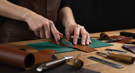 Obraz premium Close-up of hands cutting leather with knife on work table. Leather crafting project cutting hide hands at work shop for handmade goods