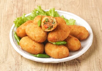 Kroket kentang. Croquettes are lumps of finely mashed potatoes filled with seasoned minced meat and mixed with vegetables such as carrots or green beans. The croquettes are coated with beaten egg and 