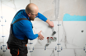 Man installing ceramic granite tiles on the wall in the new apartment. Plumber installing ceramic...