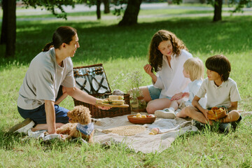 Caucasian middle aged woman sitting on picnic blanket with two children and her husband, sharing...