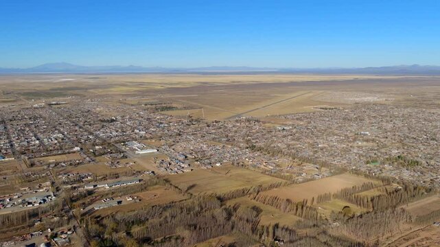 Slow wide drone glide over southern edge of Malarg&uuml;e in Mendoza province, revealing farmland patterns, town limits and vast arid plains under clear skies with distant mountain silhouettes