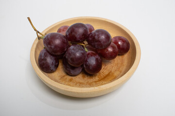 Wooden bowl filled with fresh and juicy red grapes, placed on a white background.