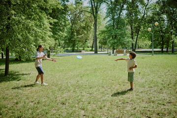 Asian middle aged man and his child playing frisbee together in park, both standing on grass...