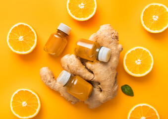 Bottles of turmeric and orange energy immune shot drink with fresh oranges slices on orange background.