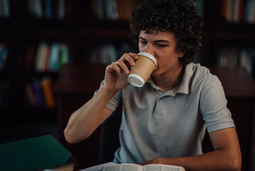 Student drinking coffee while studying in library