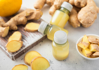 Immune ginger energy shot drink bottles with fresh raw ginger root and lemon on light background.Macro.
