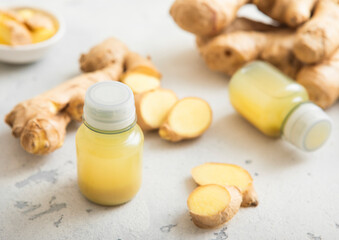 Immune ginger energy shot drink bottles with fresh raw ginger root on light background.Macro.