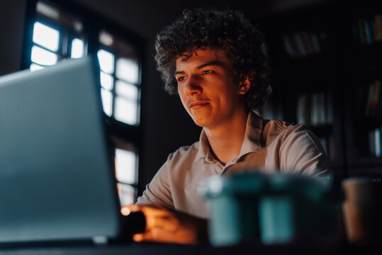 Focused young man working on laptop in home office at night
