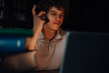 Focused student working late at night on laptop and talking on smartphone