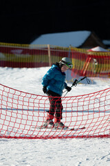 Joyful child mastering skiing skills while navigating through a vibrant red snow fence on a bright...