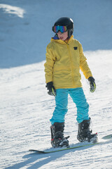 Bright yellow jacket gleams under the sun as a young snowboarder conquers the snowy slopes with...