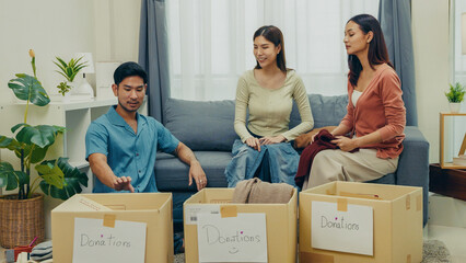 Asian friends sorting and placing clothes into cardboard donation boxes at home. Concept of...