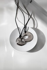 Modern Silver Handmade Pendants on Black Cord Displayed on White Dish, Minimalist Jewelry Design.
