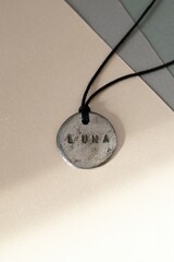 Unique Silver Pendant with Luna Inscription on Neutral Backdrop. Stylish Jewelry Photography.