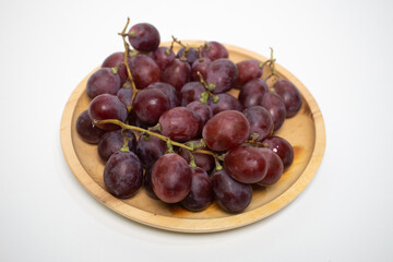 Delicious bunches of ripe purple grapes served on a round wooden tray.