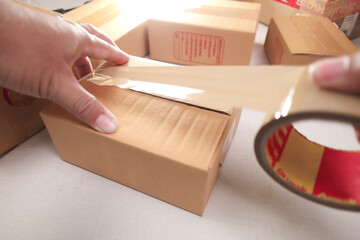 Hands sealing cardboard box with brown packing tape for shipping, surrounded by other delivery...