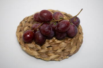 Fresh red grapes placed neatly on a rustic straw mat, ready to serve.