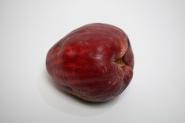 Tropical Jamaican guava fruit with deep red skin lies isolated on a clean white surface.