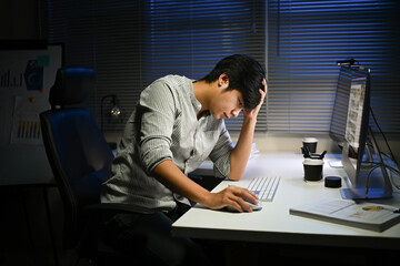 A man is sitting at a desk with a computer monitor and a keyboard. He is looking at the monitor and...