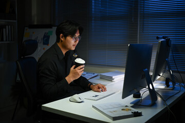 A man is sitting at a desk with a cup of coffee in front of him. He is wearing glasses and is...
