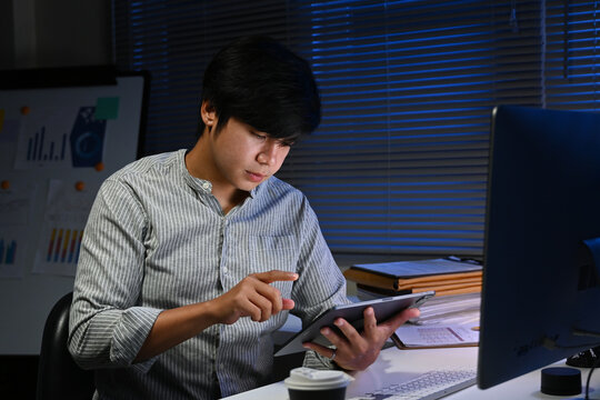 A man is sitting at a desk with a tablet in front of him. He is pointing at something on the screen