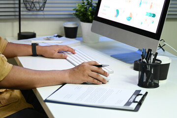 A man is typing on a computer keyboard in front of a monitor. The monitor shows a graph with a lot...