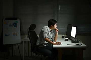 A man is sitting at a desk with a computer monitor and keyboard in front of him. He is looking at...